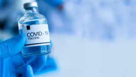 Dłoń w rękawiczce trzymająca buteleczkę ze szczepionką z napisem COVID-19