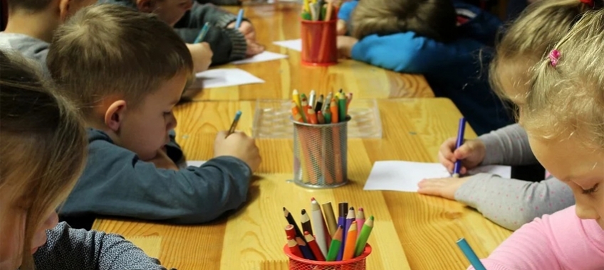 zdjęcie zawiera dzieci piszące kolorowymi kredkami na kartkach papieru